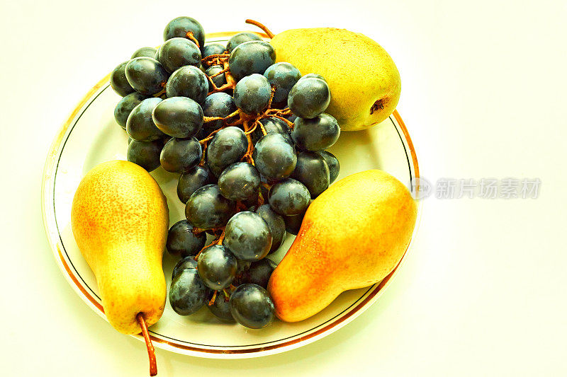 成熟可口的黄梨和黑甜的葡萄放在盘子里