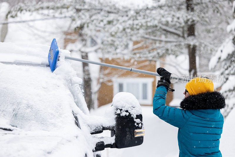 一名年轻女子在暴风雪后清理车上的积雪