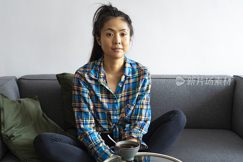 亚裔美国妇女一边看电视一边喝咖啡