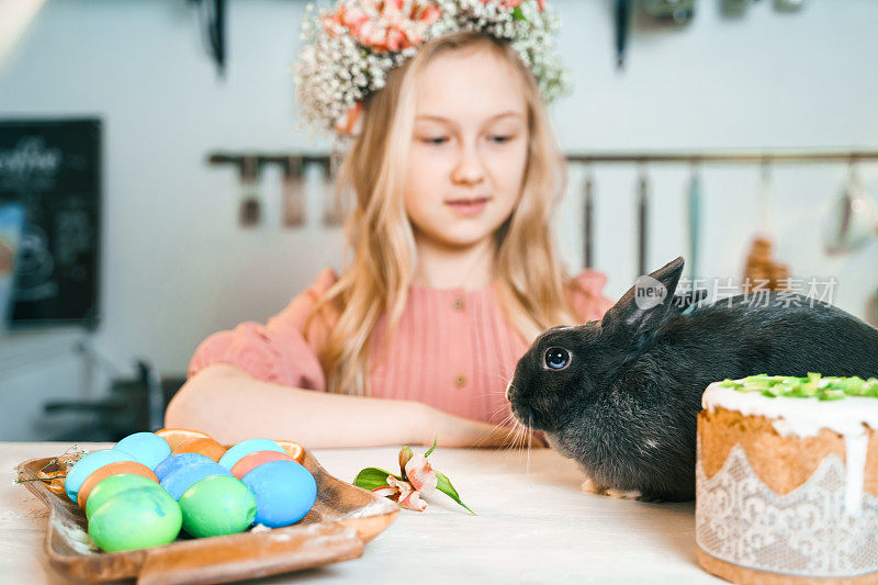 美丽的女孩头戴花环庆祝复活节。做蛋糕，在餐桌上画鸡蛋。节日快乐在一起。和复活节兔子玩，兔子