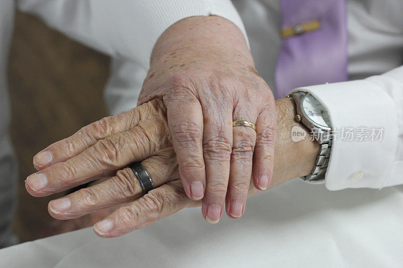 80岁的老夫妇手牵着手，展示他们的结婚戒指