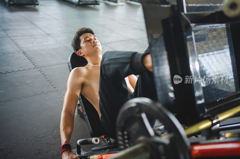 亚洲男子运动员在体育馆用器械做腿部按压练习，以增强肌肉