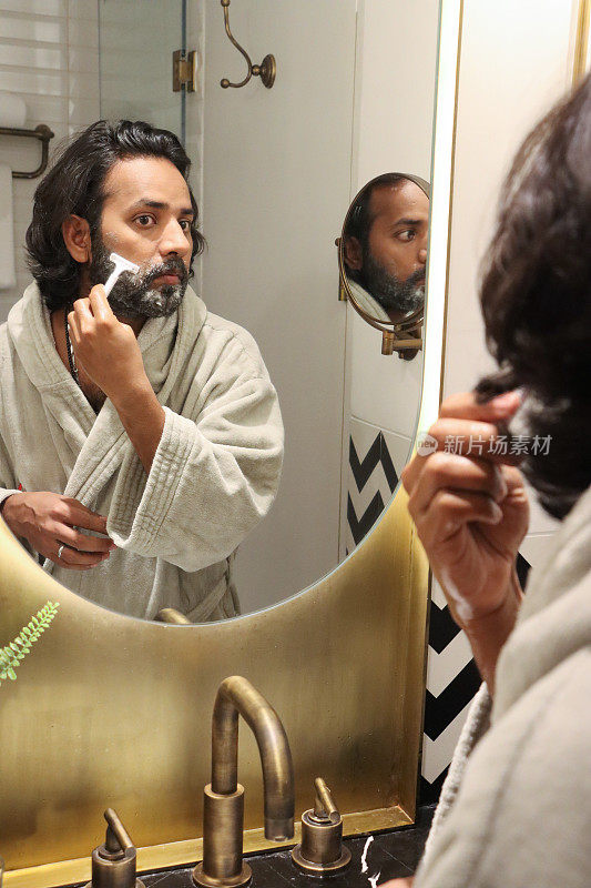 近距离反射在镜子的印度男子站在水槽浴室穿着浴袍使用剃刀修剪面部毛发，剪胡子和小胡子，自我护理和修饰概念
