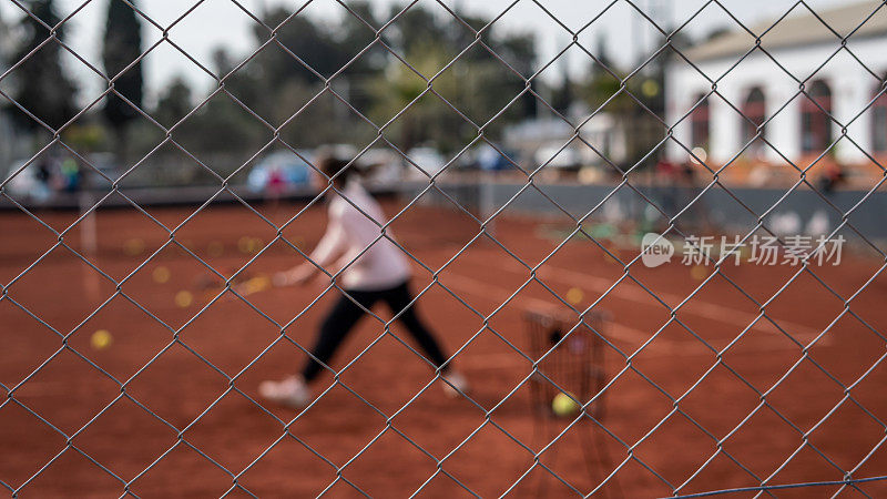 网球栅栏是前景，女子网球运动员是背景，红土场上仍是水平网球