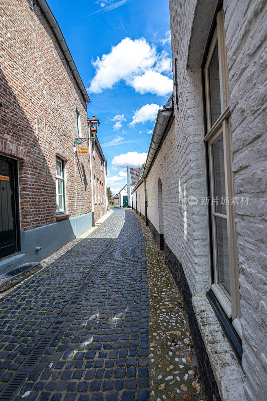 空无一人的鹅卵石狭窄街道夹在白色和砖墙的房屋之间，蓝天映衬下的城市风光