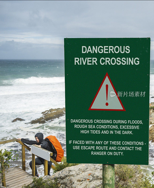 一名男子在海边徒步旅行，路过一个危险的渡海标志