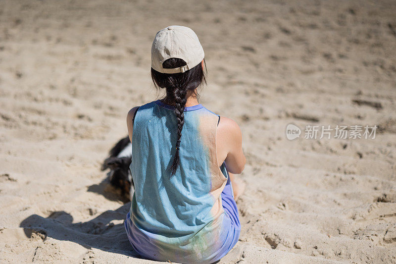 年轻女子带着狗坐在沙滩上