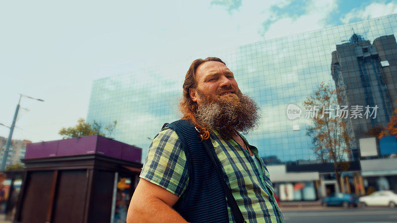 身穿格子衬衫的红发大胡子男子站在城市街道上看着镜头
