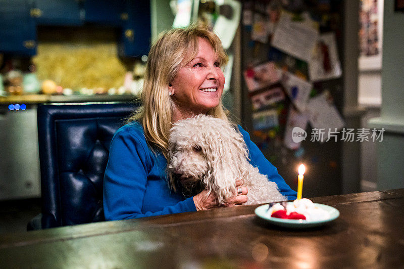 一个60多岁的成熟女人在家里吃着生日蛋糕，带着她的宠物狗过生日