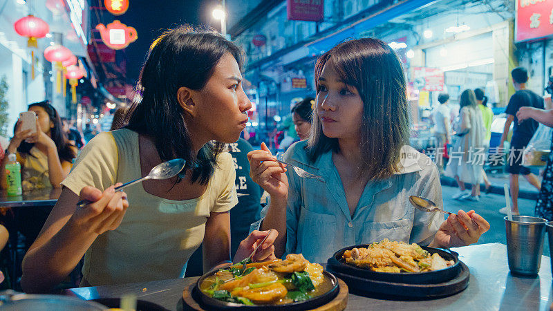 年轻的亚洲女性朋友们在泰国曼谷的夜市享受街头小吃。假日度假旅行。