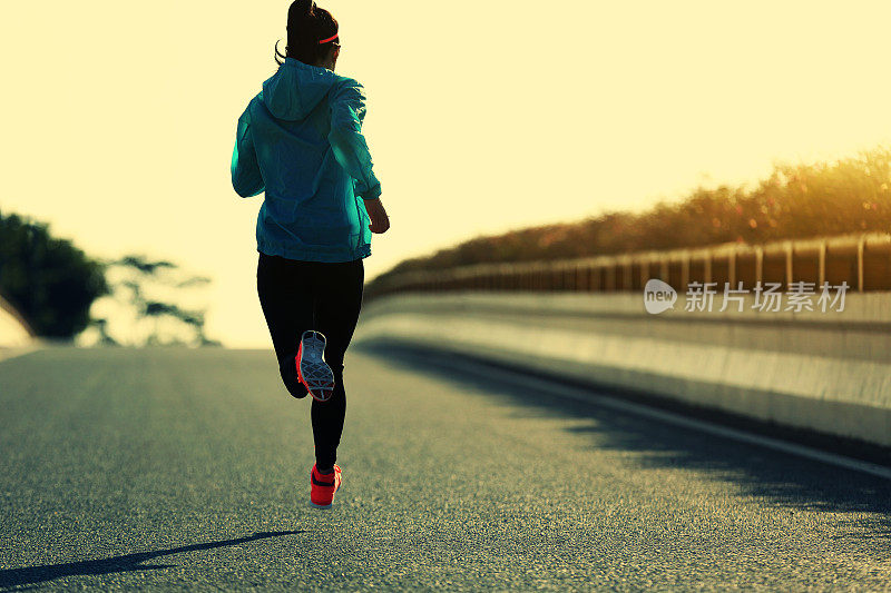 年轻的健身女运动员在日出大道上跑步