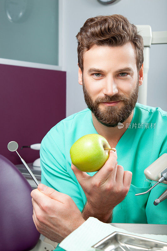 年轻英俊的男医生微笑着用白牙齿拿着苹果