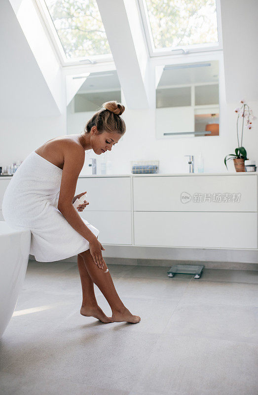 洗澡后在腿上涂抹保湿霜的女人。