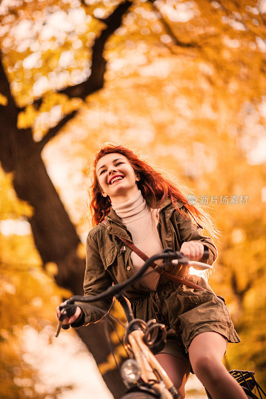 微笑的年轻女子在秋天骑自行车。