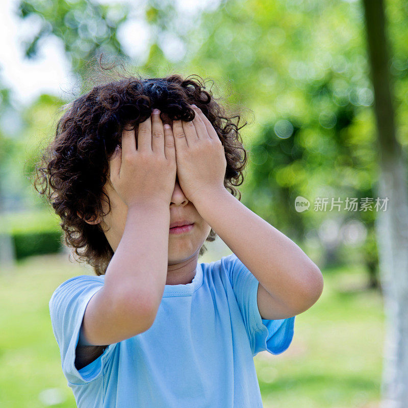 一个亚洲小男孩在公园捂着眼睛