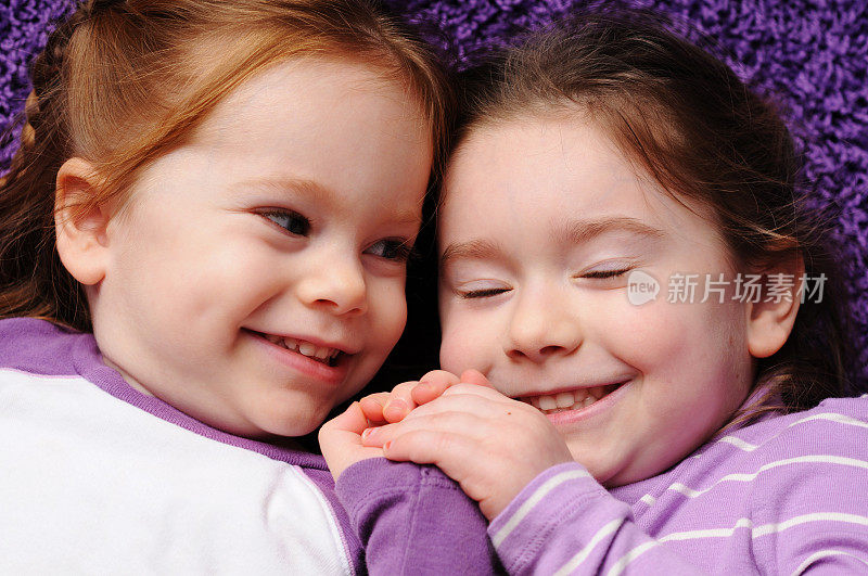 两个顽皮的姐妹躺在紫色的地毯上