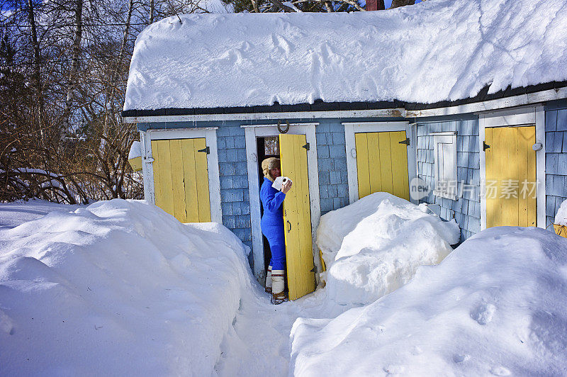 成熟的女人在冬天的雪地里走向户外厕所。