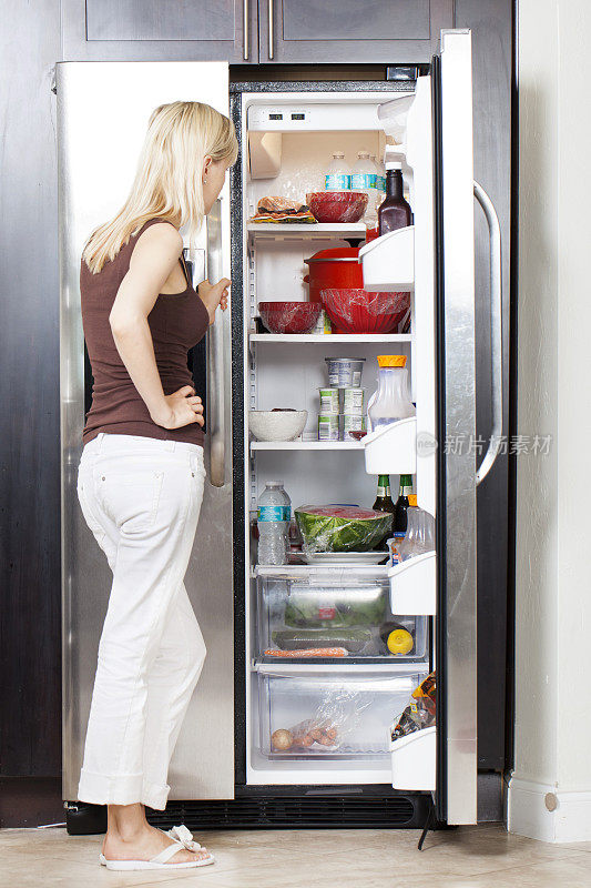 年轻女子从打开的冰箱中挑选食物