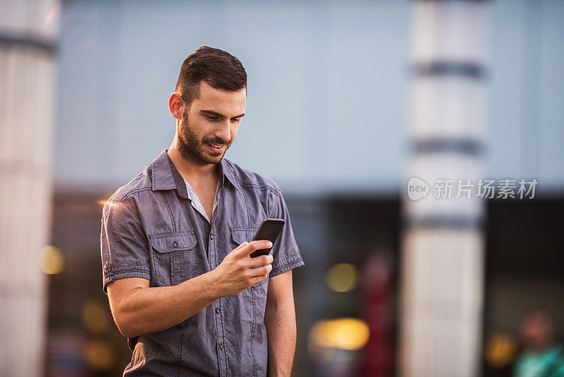 年轻快乐的商人在户外用智能手机发短信。