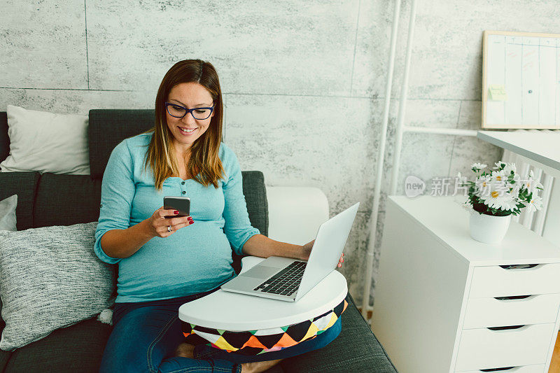 怀孕的女商人在家庭办公室用智能手机发短信。