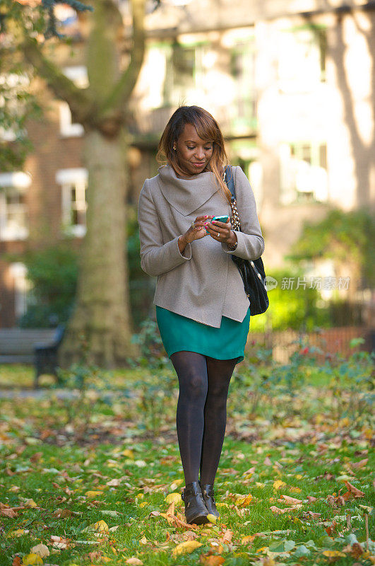 一名年轻女子一边穿过公园一边发短信