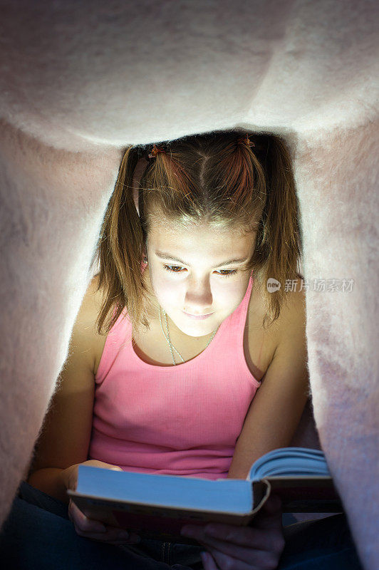 年轻开朗的女孩躲在毯子下面，全神贯注地看书