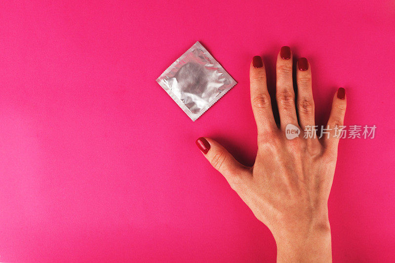 粉红色背景上的女人拿着避孕套。性保护的概念