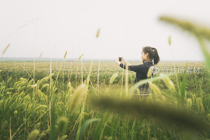 疲惫的女孩用智能手机在草地上拍摄美丽的风景