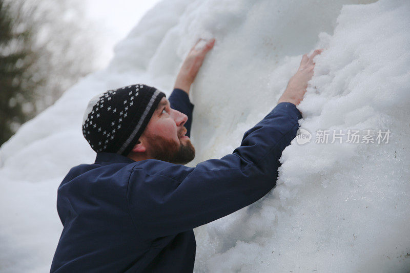 戴着帽子的大胡子男人爬上高高的雪堤