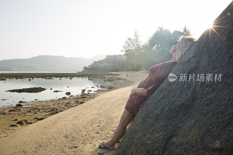 女人靠在海滩上的岩石上。