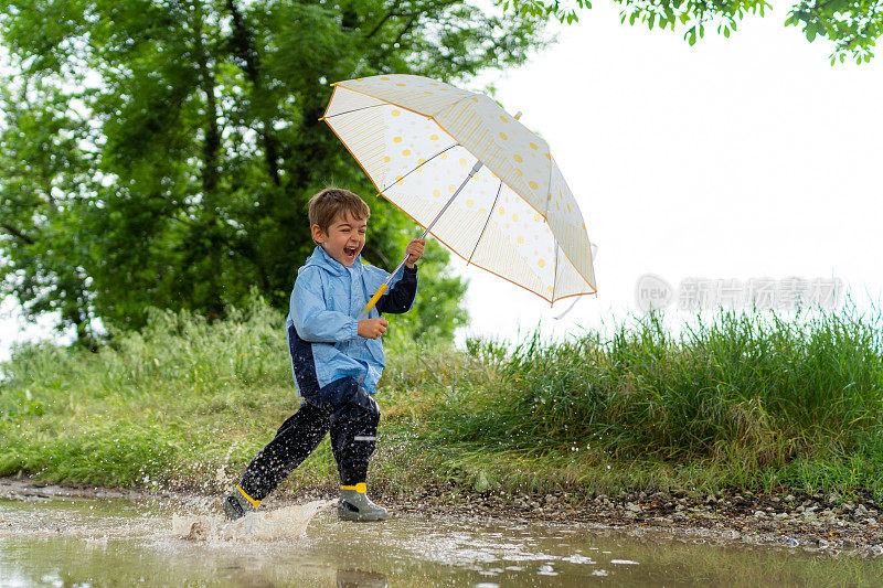 快乐的小男孩带着伞跑过雨坑