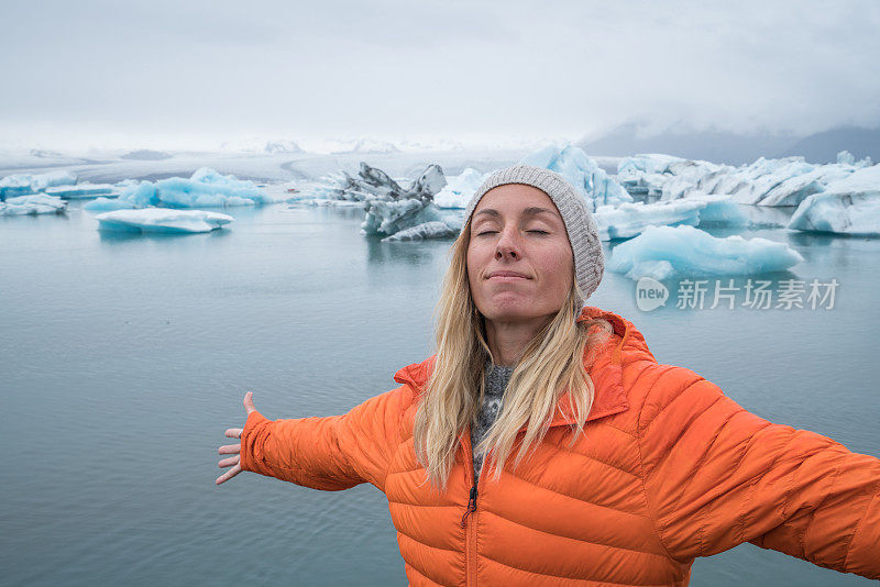 年轻女子在冰岛的冰川泻湖伸出双臂，表达自由和热爱自然的概念