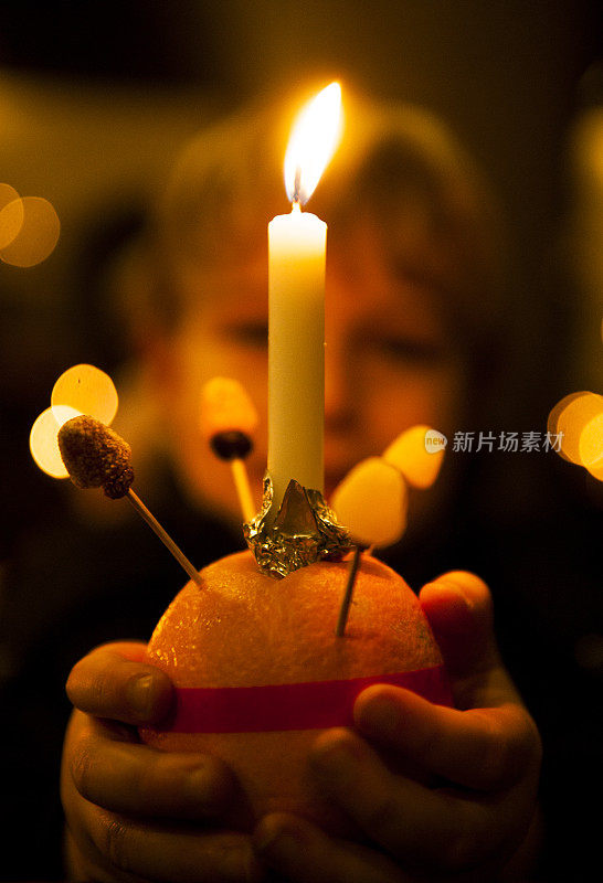 一个金发小男孩手拿克里斯汀橙色蜡烛，深色背景庆祝基督降临节