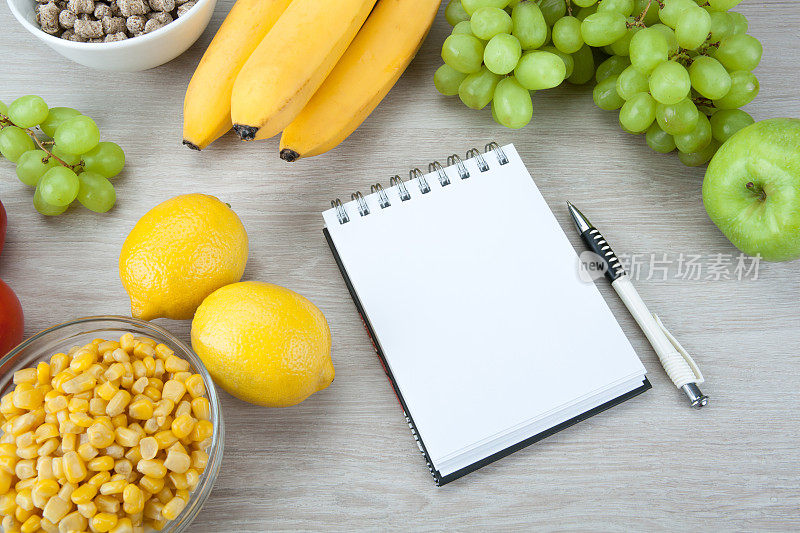 笔记本上有一个饮食计划，在桌子上靠近一些新鲜的蔬菜和水果