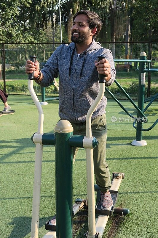 印度男子在户外健身房里使用十字骑手健身器材，在露天公园里锻炼