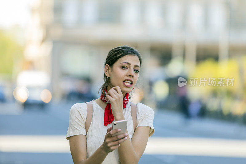 一名年轻女子正带着她的智能手机走在城市的路上