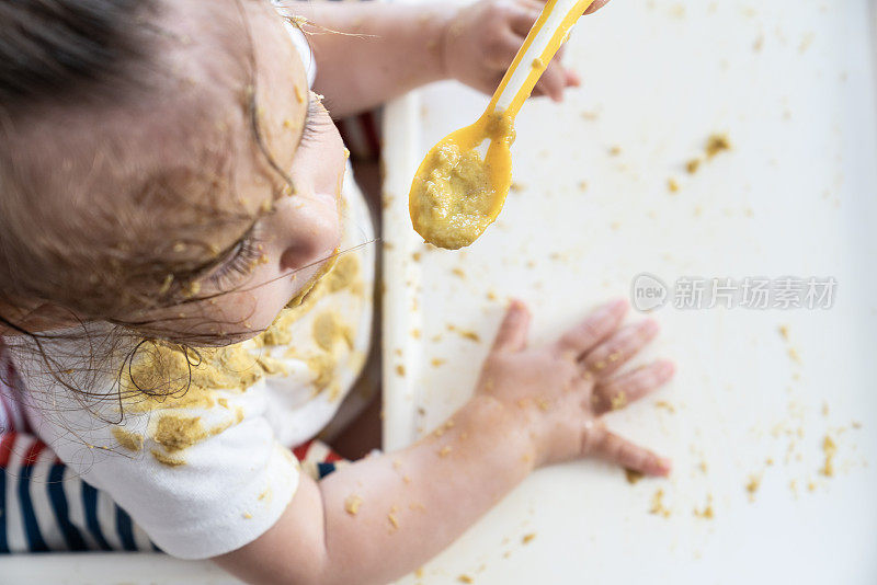 女婴在喂食椅上吃东西的高角度照片