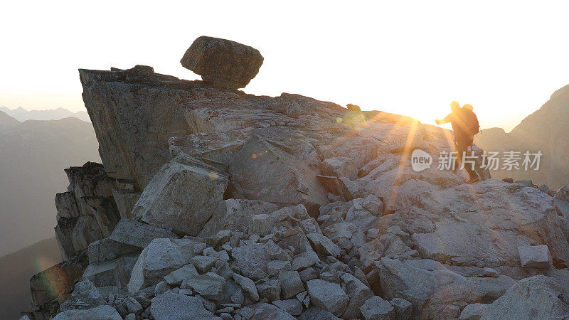 登山者在日出时徒步爬上岩石的顶峰