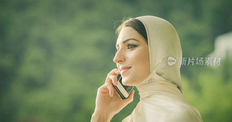 年轻迷人的穆斯林女性在hijab打字电话的特写肖像