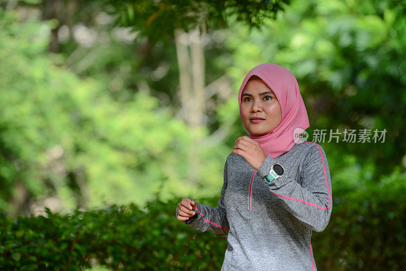 年轻的亚洲穆斯林女运动员戴着智能手表在慢跑跑道上跑步