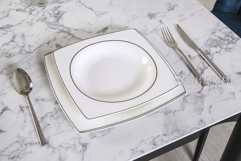 刀叉平铺在朴素的餐巾上，桌上放着白色的空盘子，大理石桌上