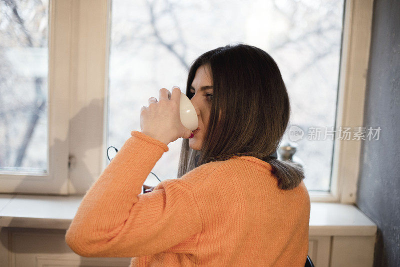 美丽的年轻女子，早上在窗边喝咖啡