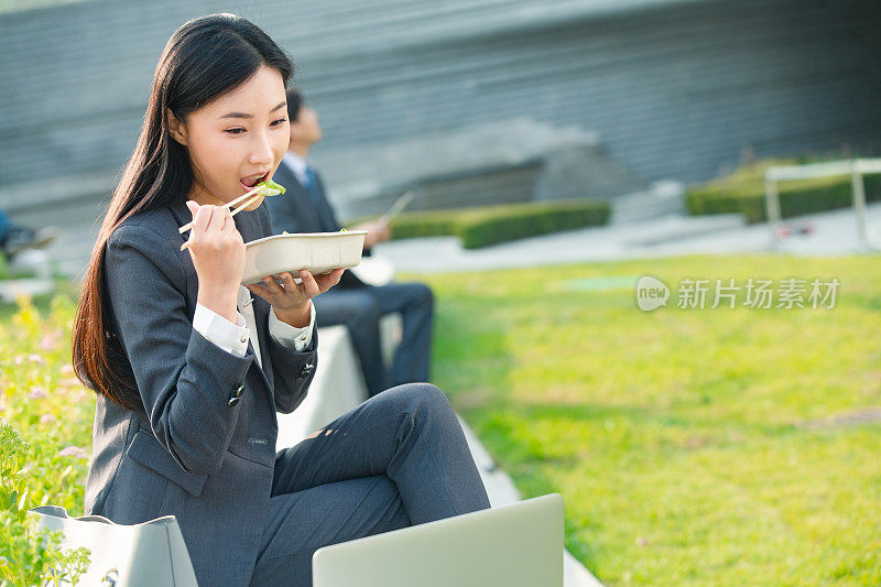 商务女性坐着户外边吃饭边工作