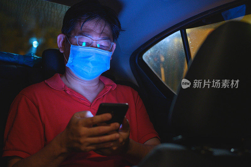 亚洲男性乘客在出租车内使用智能手机时戴上口罩