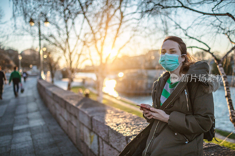 妇女使用手机和保护面膜在户外