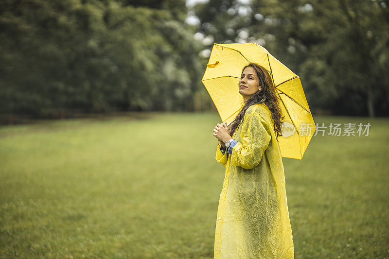 女人穿着雨衣，撑着雨伞，在雨天行走