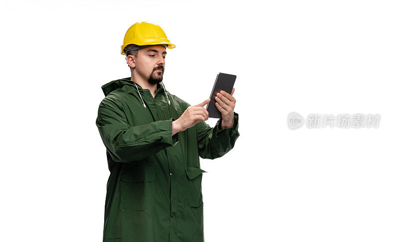 身穿绿色雨衣、头戴安全帽的工程师在白色背景下使用数码平板电脑