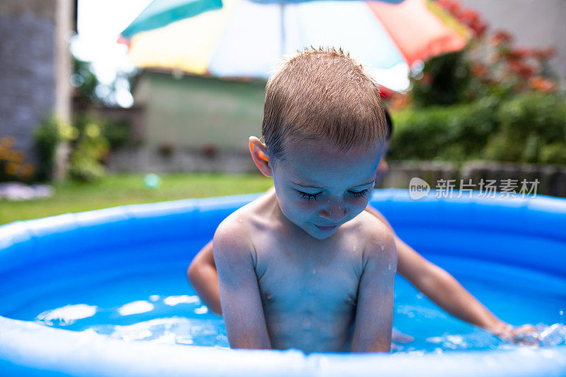 一个金发小男孩坐在一个嬉水池里