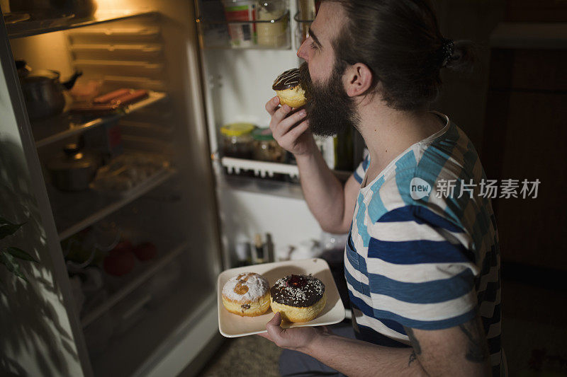 大胡子男人在冰箱前吃甜甜圈