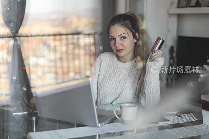 一个年轻漂亮的女人用信用卡在网上购物。一个拿着信用卡用笔记本电脑的少女。网上购物的概念